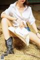 A woman in a white shirt and cowboy hat sitting on hay.