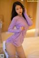 A woman in a purple dress is posing on a bed.