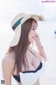 A woman in a black bikini and a straw hat on the beach.
