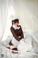 A woman in a maid outfit sitting on a bed.