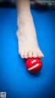 A person's foot on a pool table with a red ball.