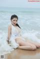 A woman in a white bikini sitting on the beach.