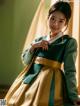 A woman in a green and gold hanbok poses for a picture.