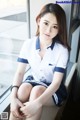 A woman in a school uniform sitting on a window sill.